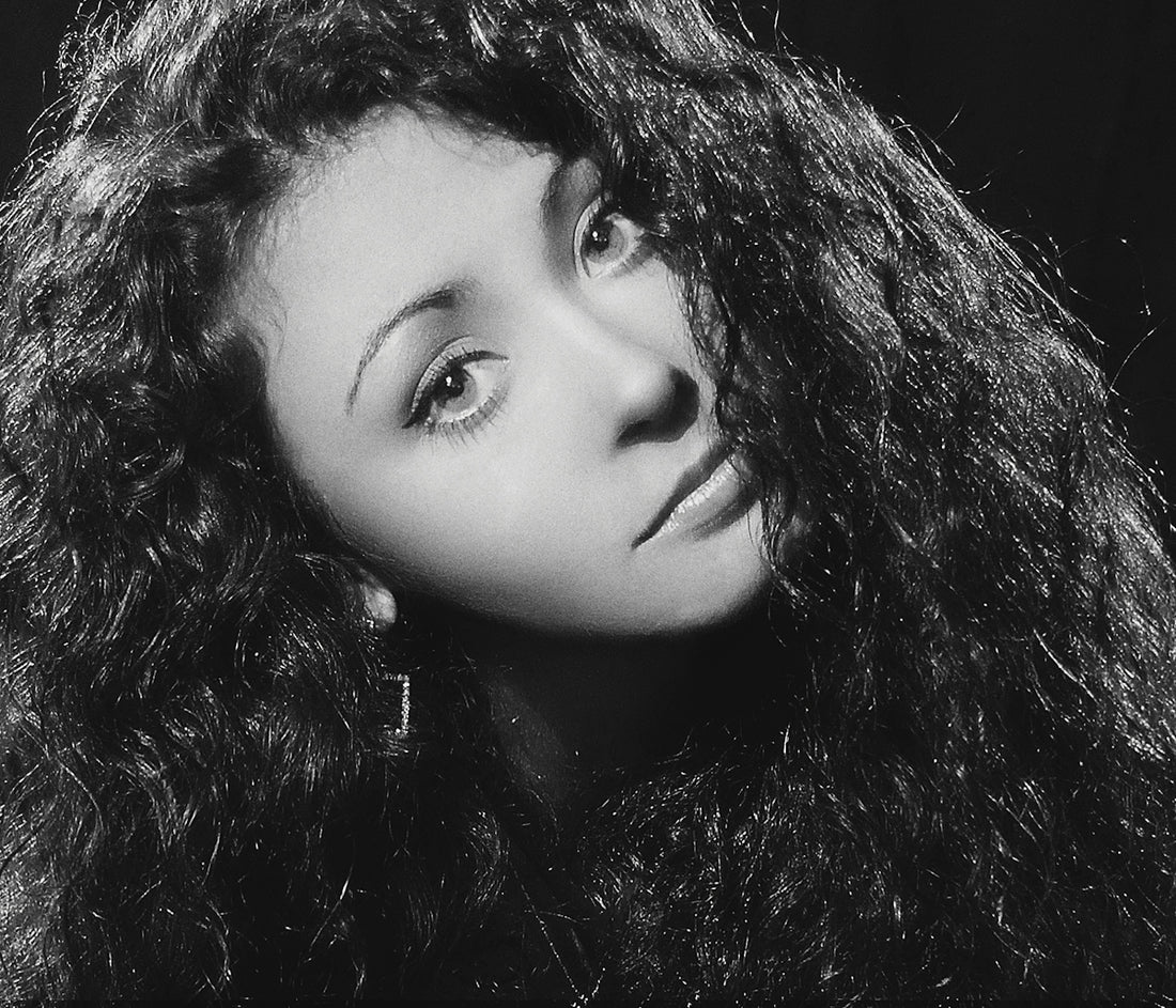 A young woman with curly hair poses elegantly.