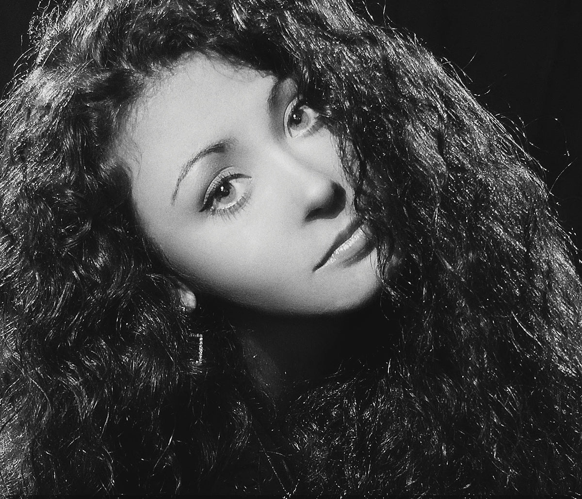 A young woman with curly hair poses elegantly.