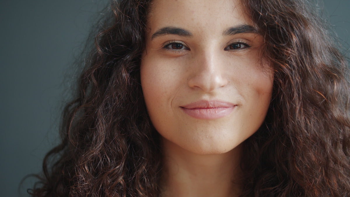 Young woman with curly hair smiles softly.