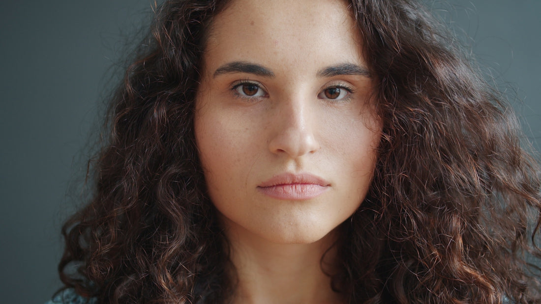 A young woman with curly dark hair looks forward.
