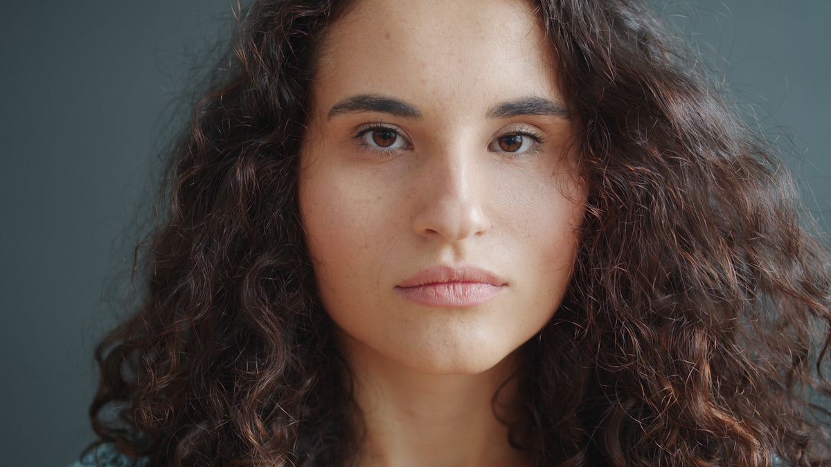 A young woman with curly dark hair looks forward.
